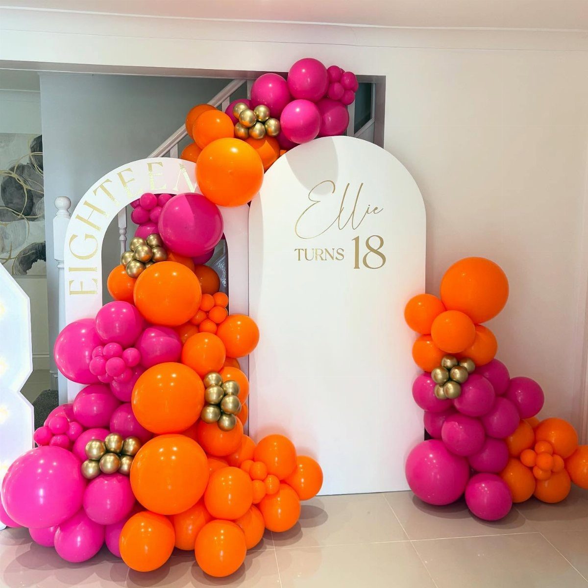 Pink and orange balloon garlands surrounding white arched backdrops for an 18th birthday.