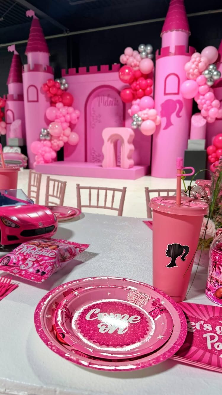 Pink castle backdrop with balloons, plates, and a toy car for a party.
