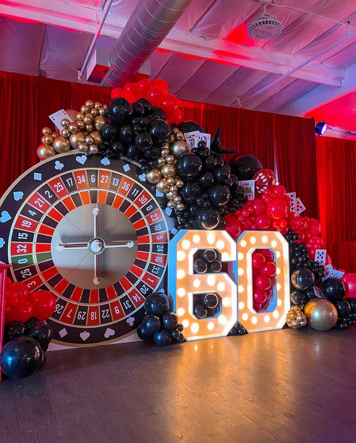 Casino themed party decor with a roulette wheel, gold balloons, and glowing 60 numbers.