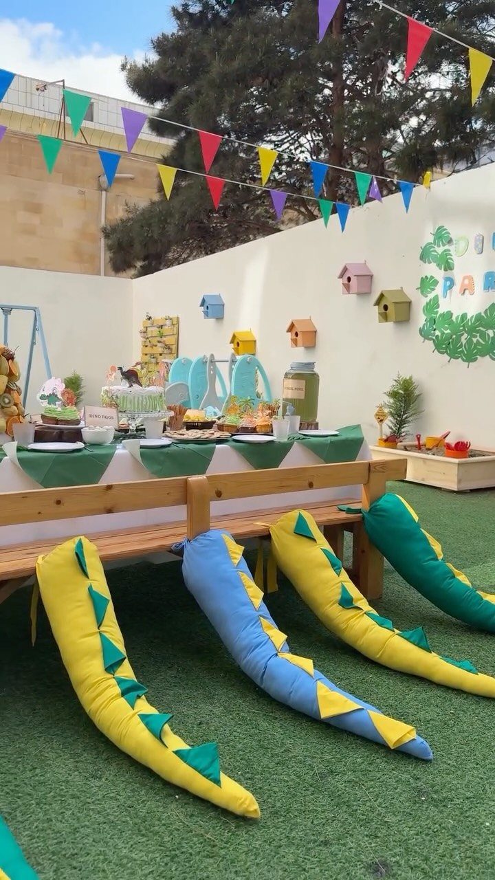 Dinosaur themed party setup with colorful fabric dinosaur tails attached to wooden benches.