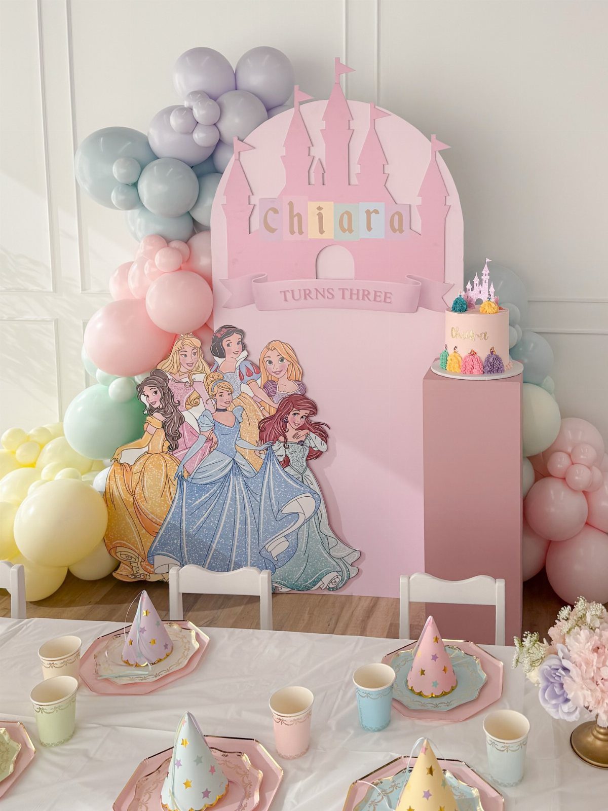 Disney princess birthday party setup with pink castle backdrop, balloons, and table settings.