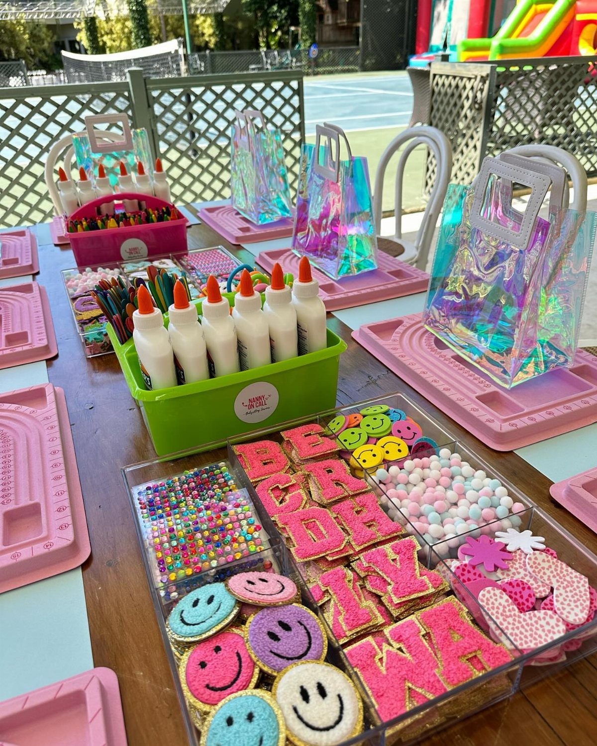 Craft station with iridescent bags, glue, markers, and glittery letters on a table.