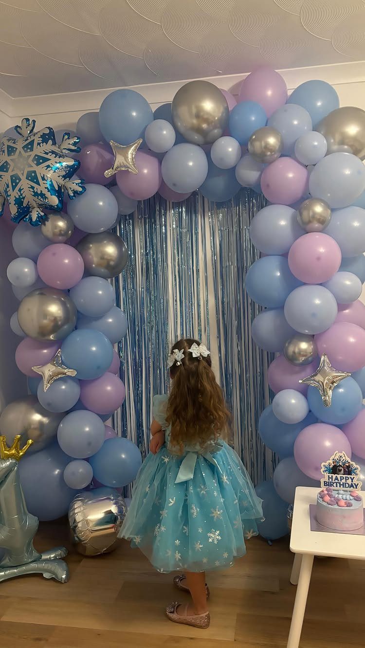 Girl in blue sparkly dress standing before a blue and purple balloon arch.