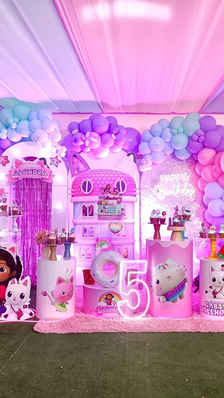 Gabby's Dollhouse birthday party setup with pink decorations, balloons, and a large dollhouse.