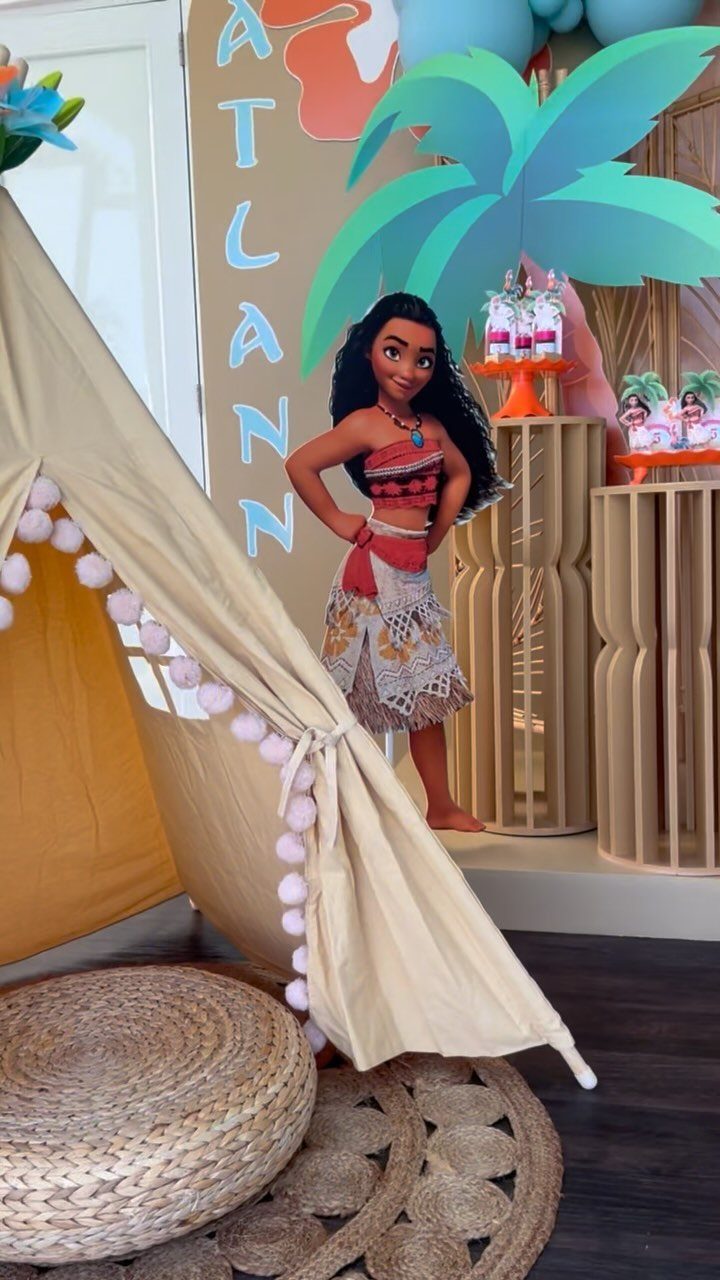 Moana cardboard cutout standing next to a beige teepee and tropical party decorations.