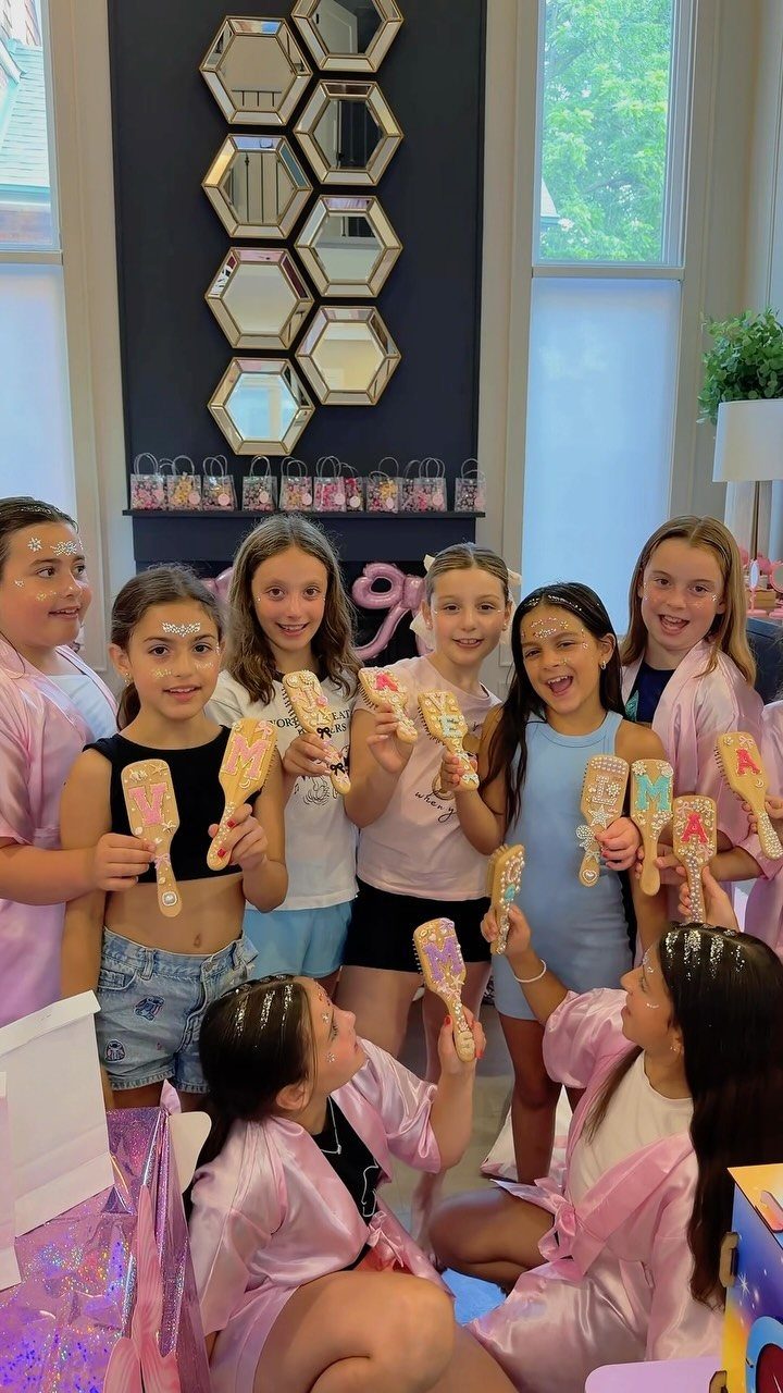 Group of young girls in pink robes holding colorful mirrors at a spa party.