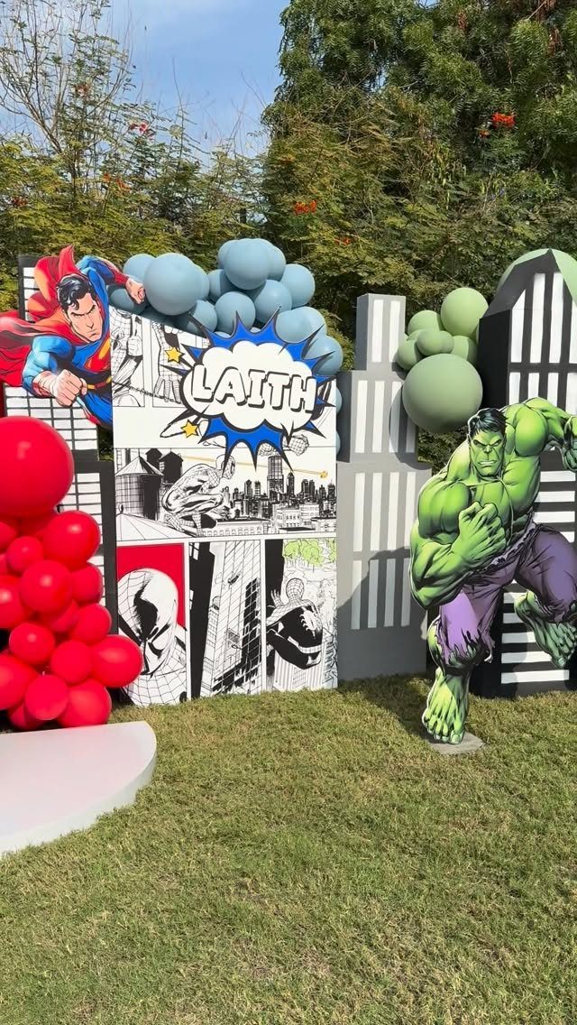 Superhero party decorations with Hulk and Superman cutouts, comic backdrops, and balloons.