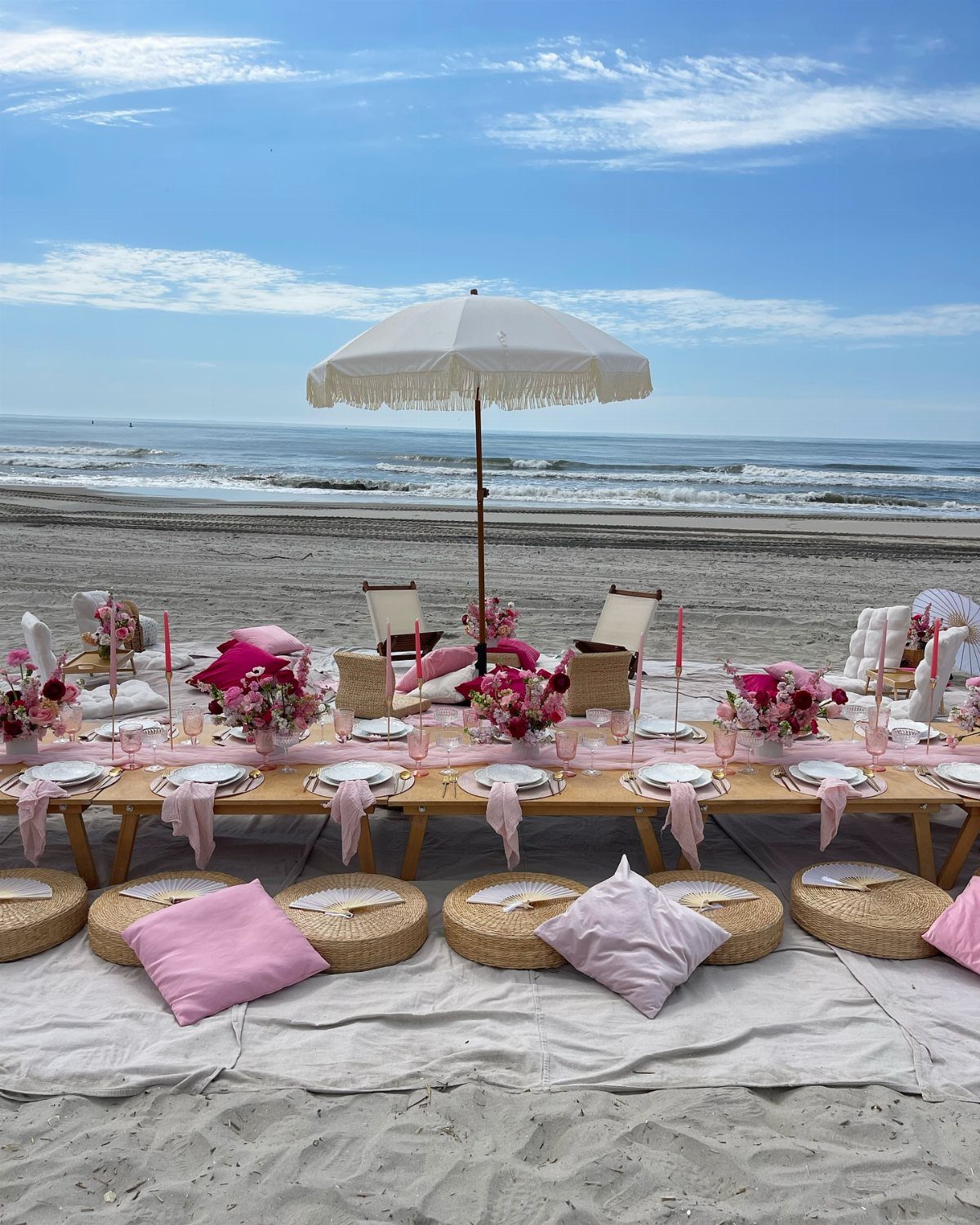 Elegant beach party setup with a long decorated table and floor cushions.