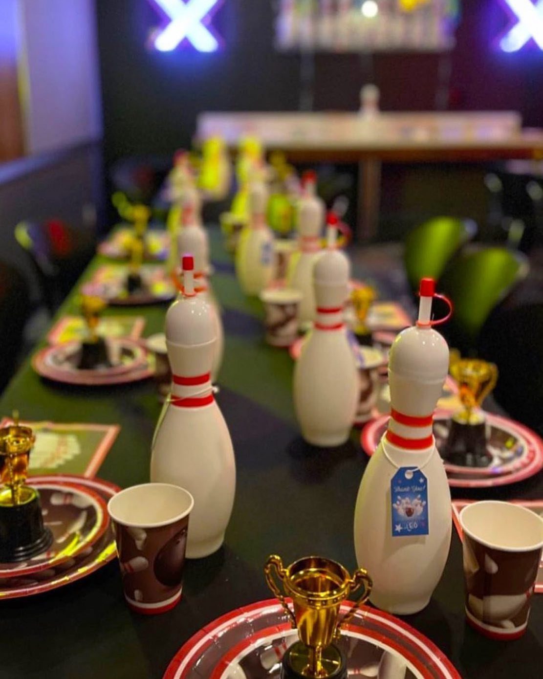Bowling themed party table setting with pin containers, gold trophies, and red plates.