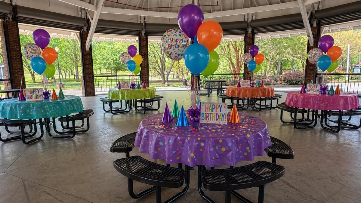 Decorated party tables with colorful balloons under a covered outdoor park pavilion.