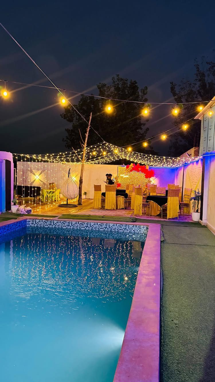 Outdoor party setup with a swimming pool, yellow tables, and glowing string lights.