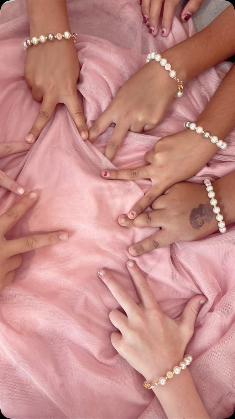 Hands of friends wearing matching white pearl bracelets resting on pink fabric.