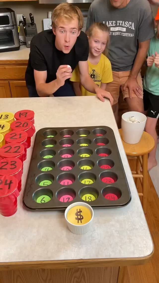 People playing a homemade game with a muffin tin and numbered cups on a counter