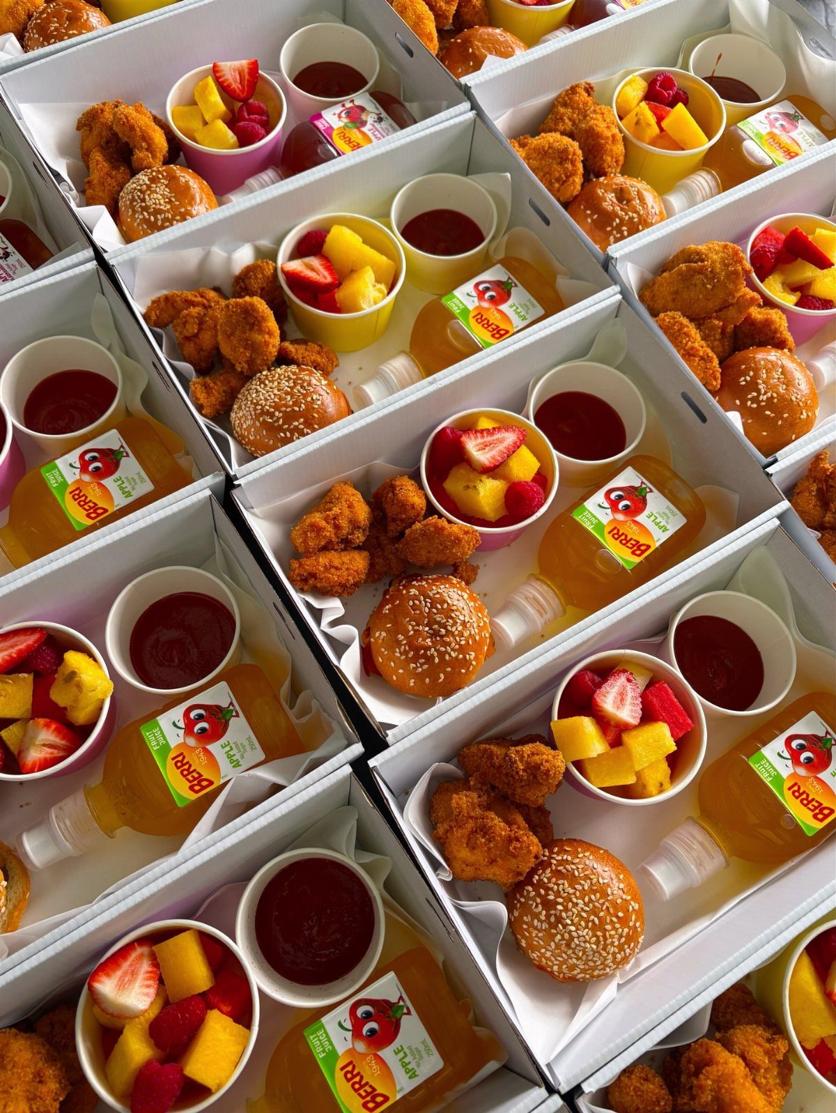 Meal boxes with chicken nuggets, buns, fruit, dipping sauce, and orange juice bottles.