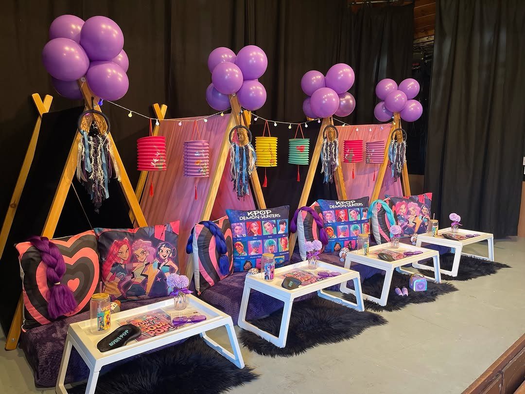 Pink teepee tents with purple balloons and colorful pillows for a slumber party.