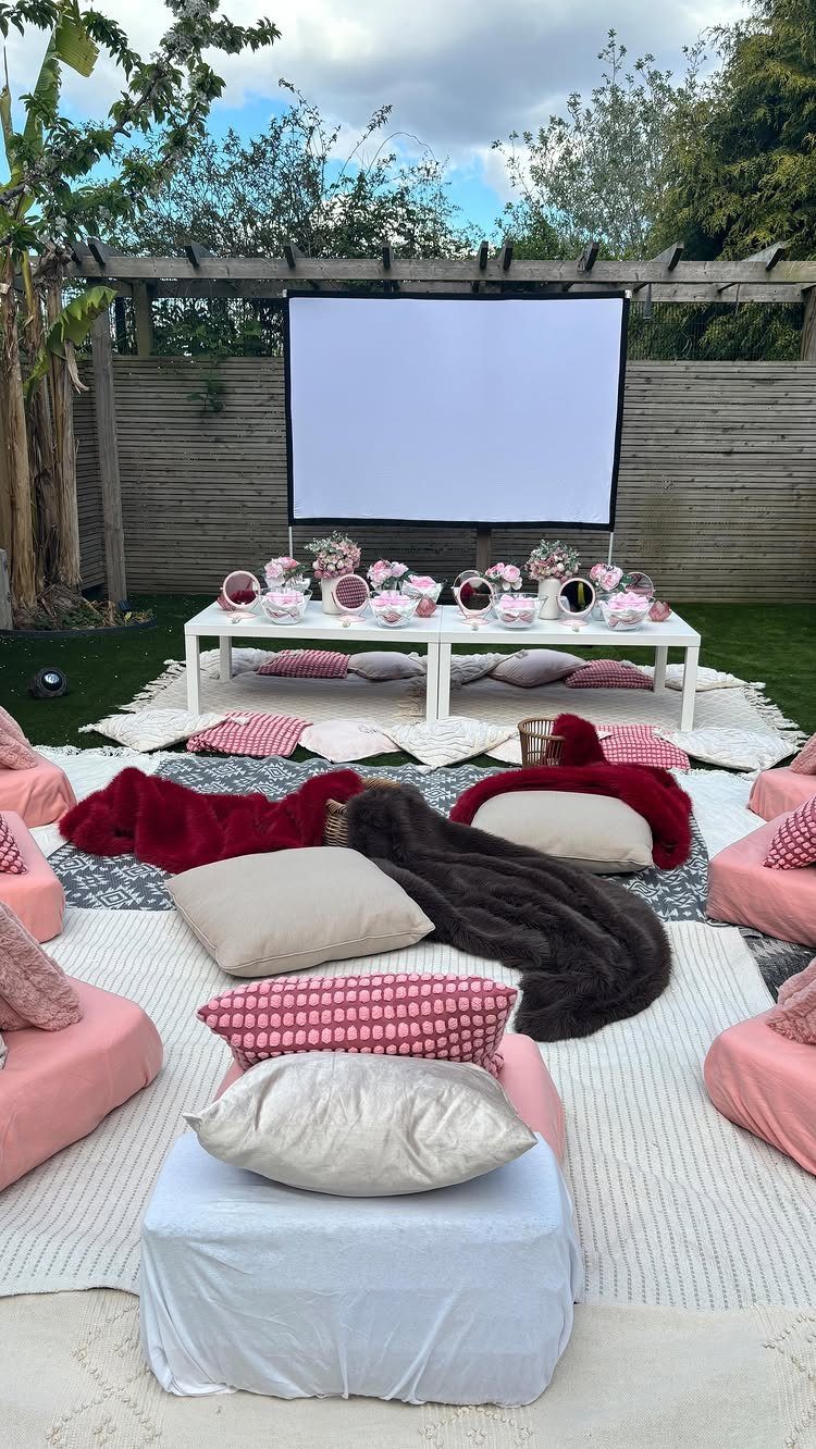 Outdoor movie setup with a projector screen, pink pillows, and a treat table.