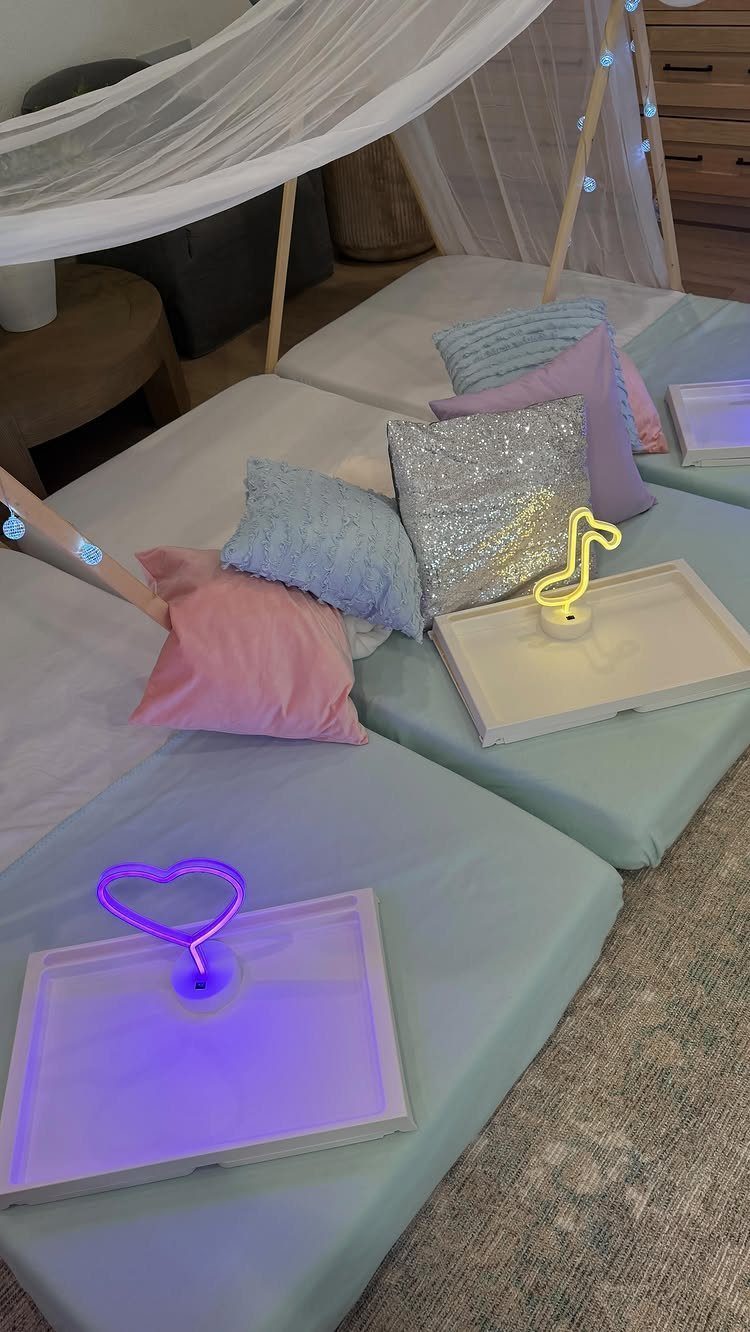 Sleepover setup with pastel pillows, neon lights, and a white canopy over mattresses.