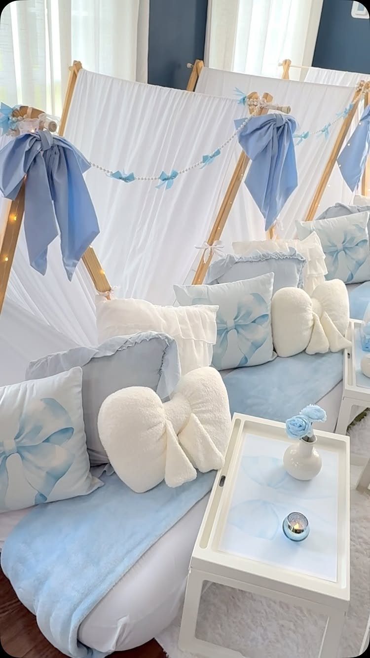 White A-frame tents with blue bows, pillows, and blankets for a sleepover party.