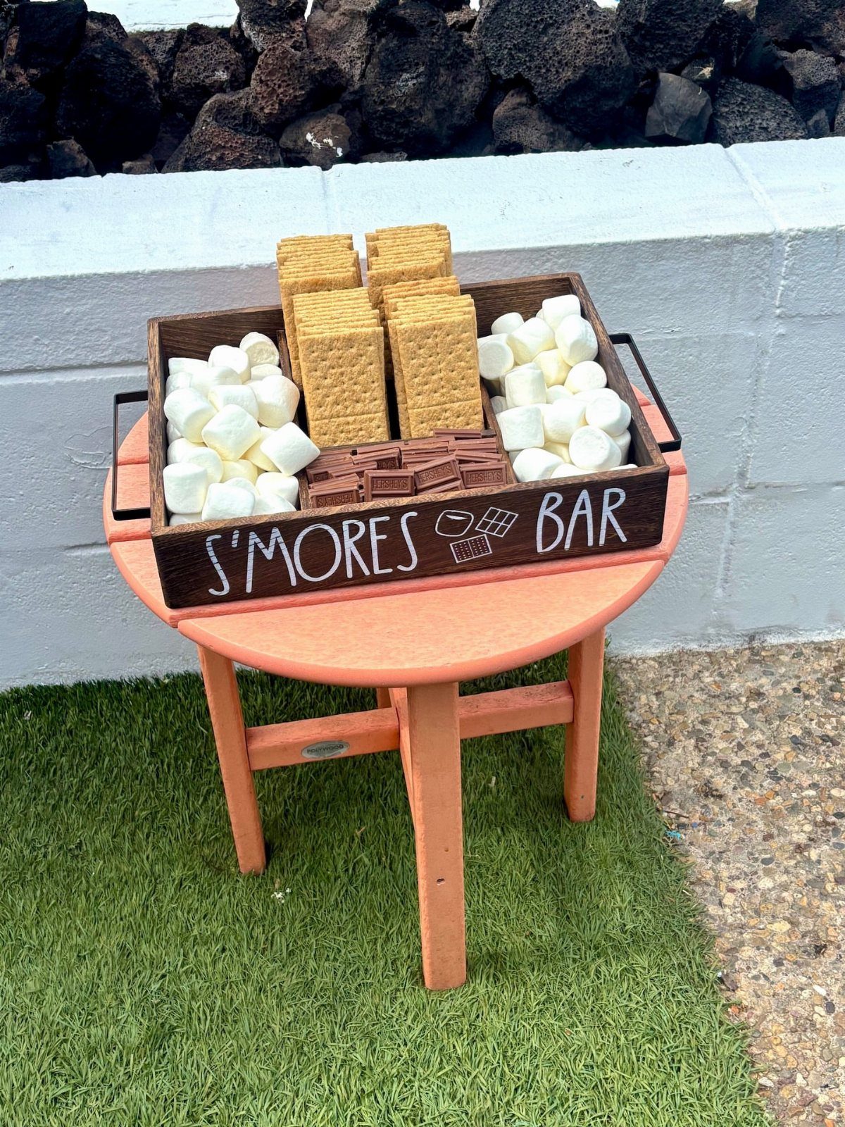 S'mores bar tray with graham crackers, marshmallows, and chocolate on an orange table.