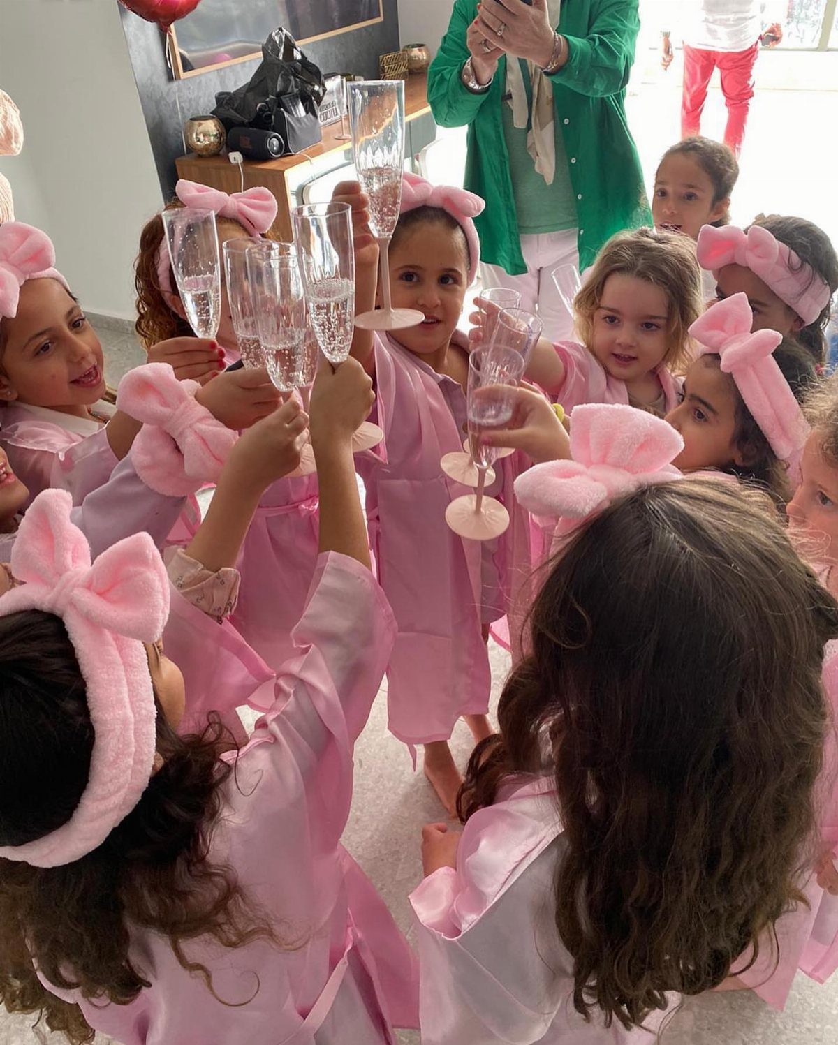 Girls in pink robes and headbands cheering with bubbly drinks for a spa party.