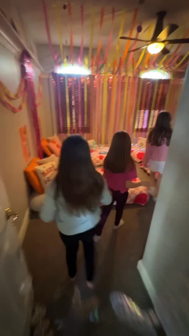 Three girls entering a bedroom decorated with colorful streamers and floor bedding.