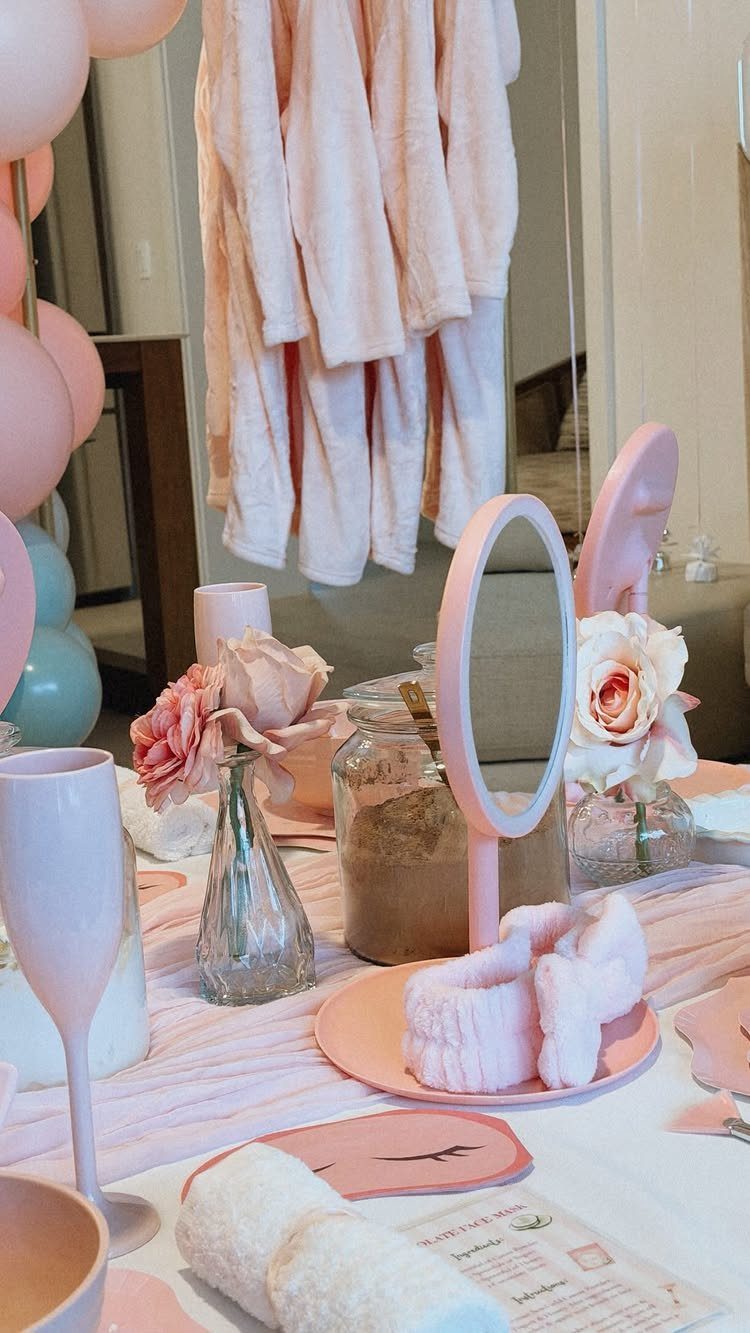 Pink spa party decorations with plush robes, roses, and towels on a table.