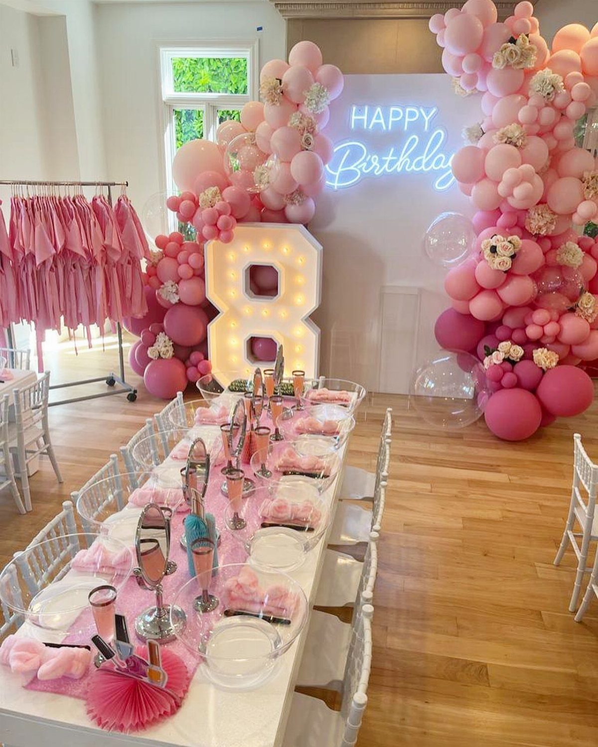 Pink birthday party setup with a large glowing number 8 and balloon arch.