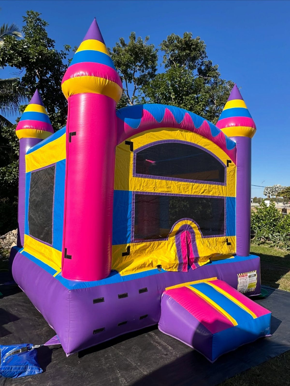 Colorful inflatable castle bounce house with pink and purple turrets on a lawn