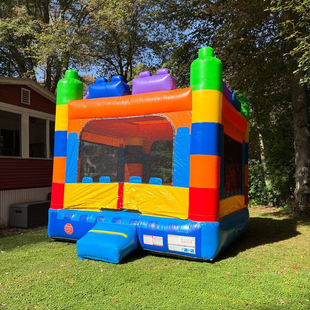 Colorful inflatable bounce house shaped like building blocks on a green grassy lawn.
