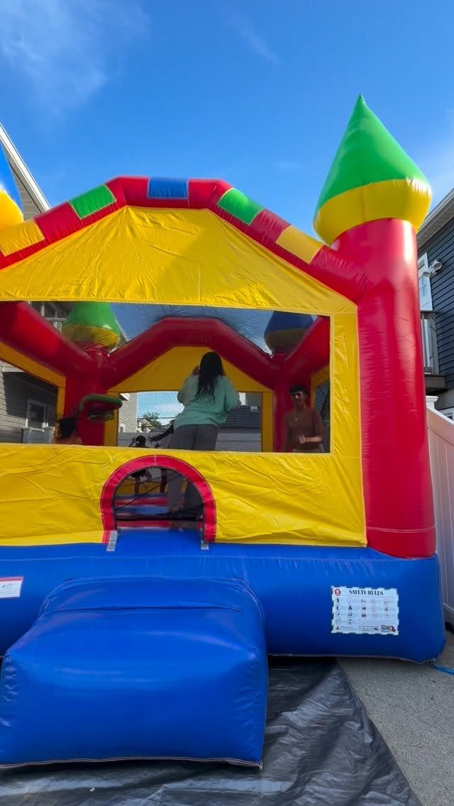 Colorful inflatable bounce house castle with people playing inside on a sunny day.