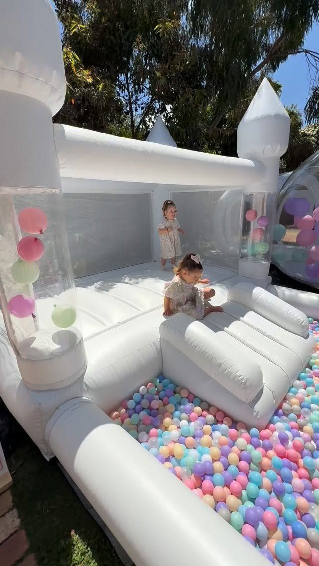 White inflatable bounce house with a slide and colorful ball pit for children.