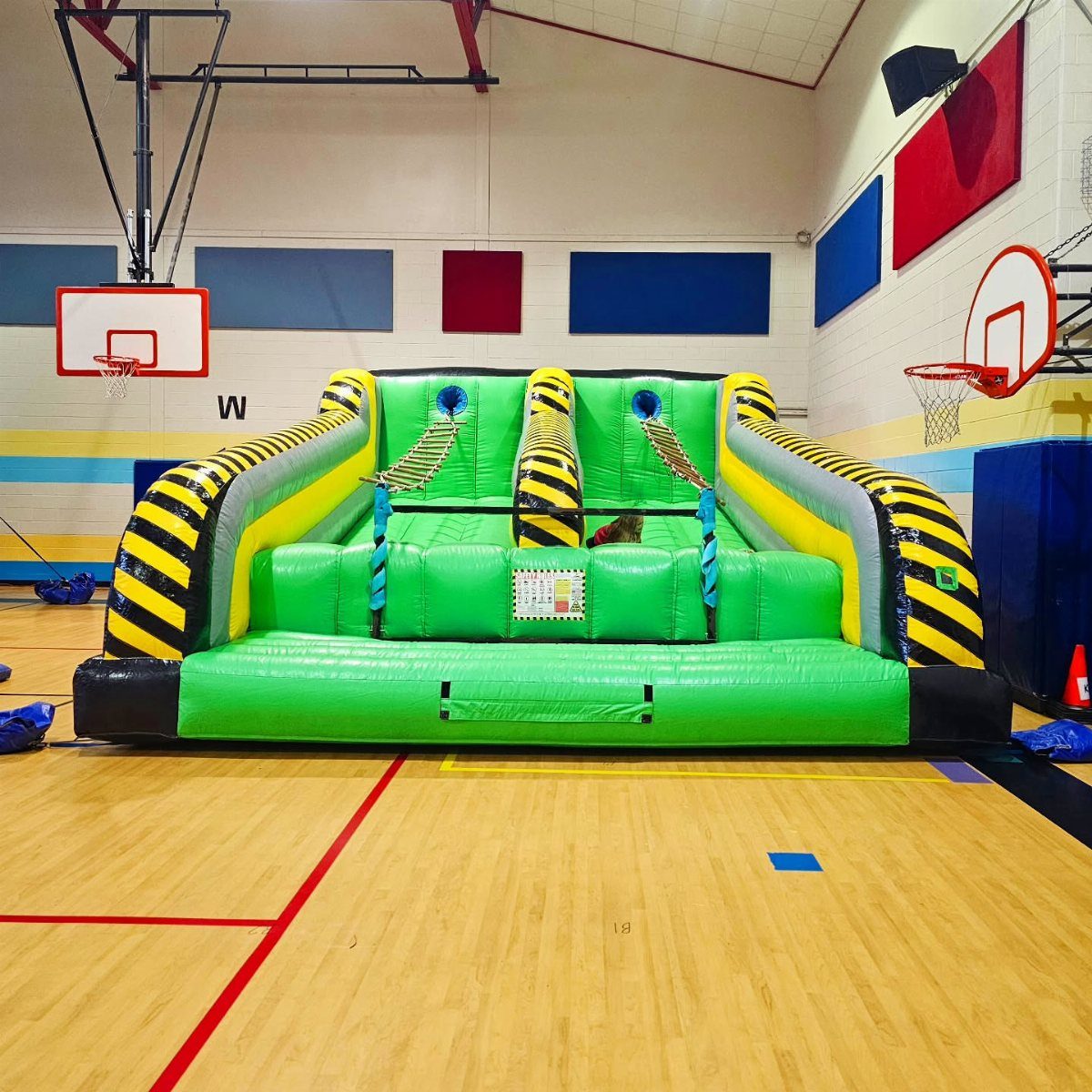 Green and yellow inflatable bounce house set up on a wooden gymnasium floor.