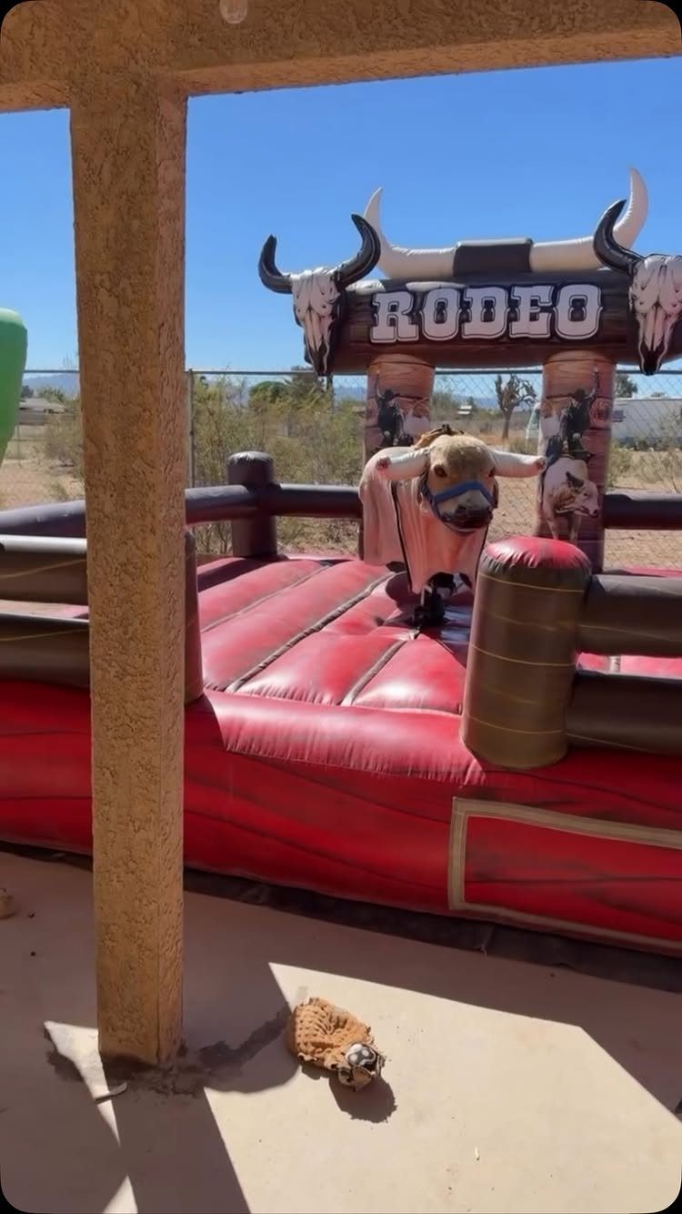 Mechanical bull ride with red inflatable base and rodeo sign outdoors.