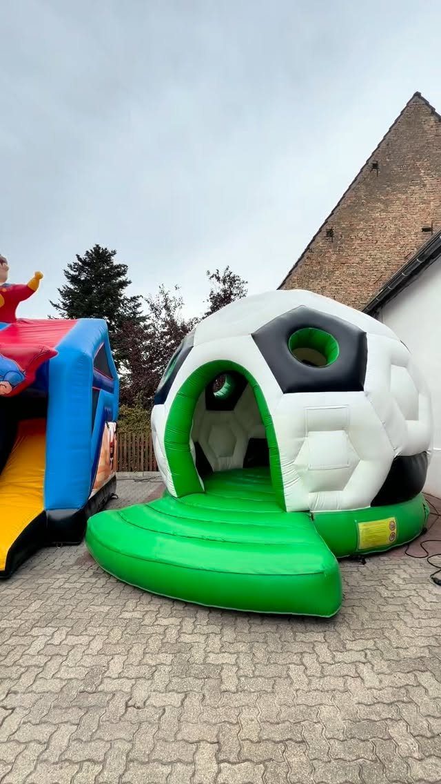 Soccer ball shaped inflatable bounce house on a grey cobblestone driveway.