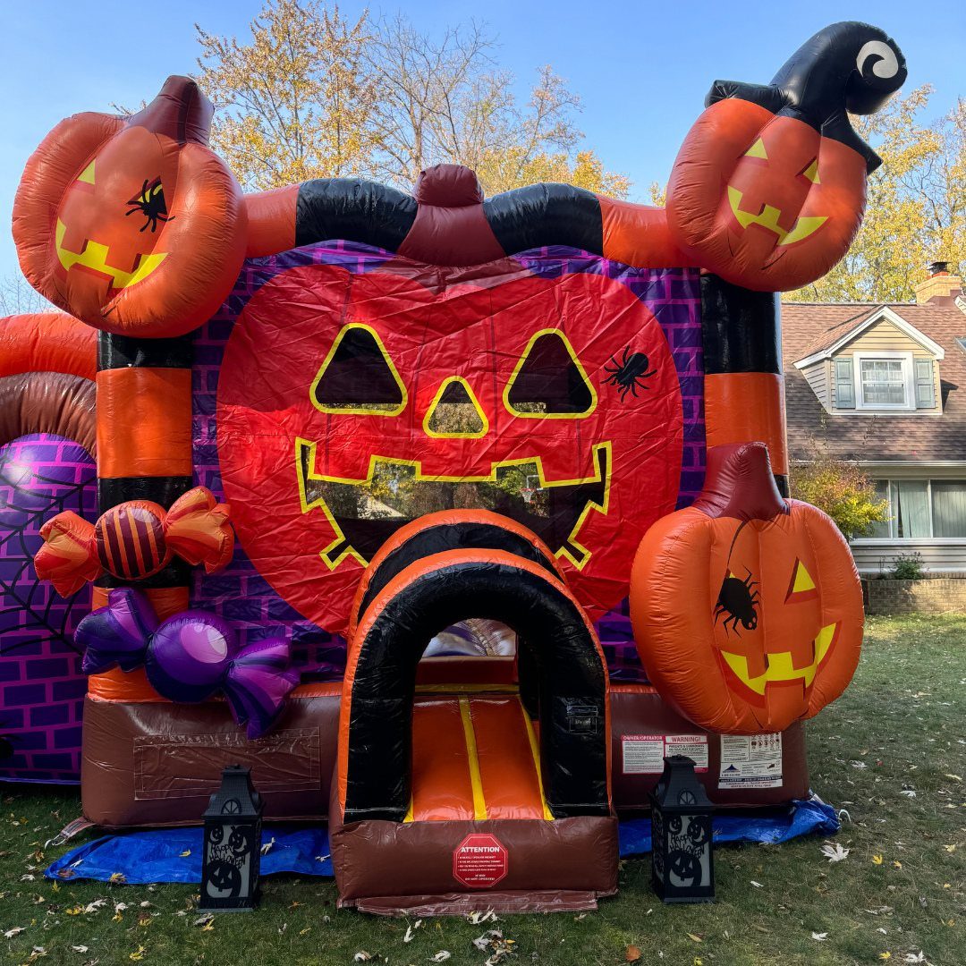 Halloween themed inflatable bounce house with pumpkin faces on a green lawn