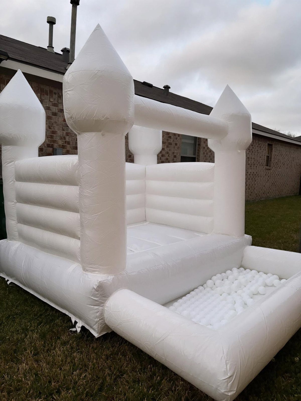 White inflatable toddler bounce house with a ball pit on a grassy lawn.