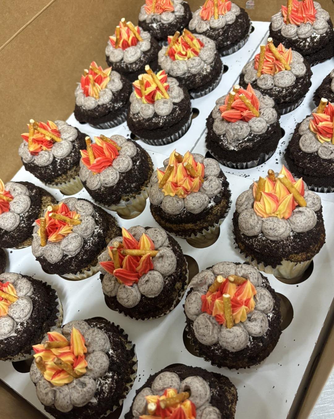 Chocolate cupcakes decorated with grey frosting stones and orange frosting flames like campfires.