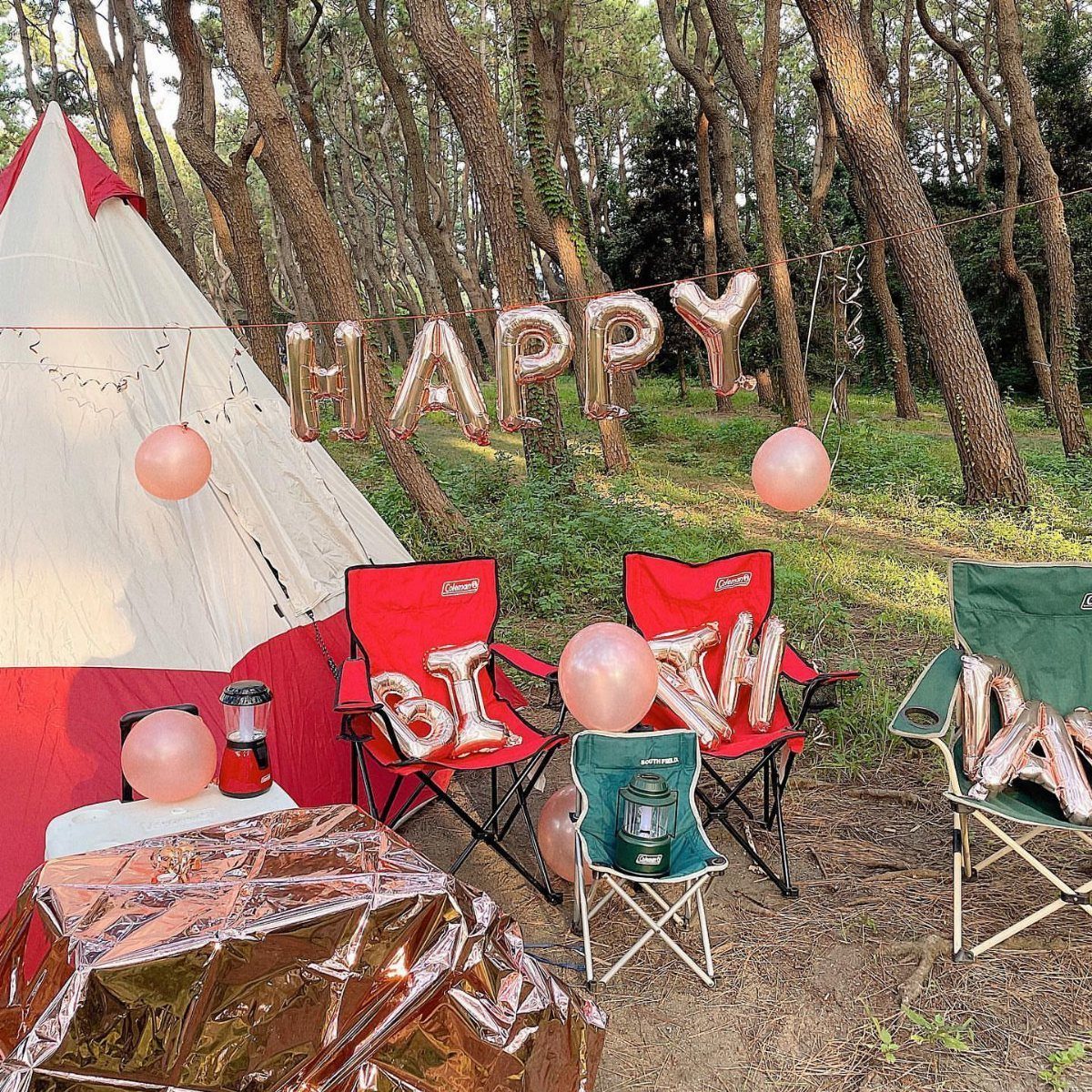 Camping birthday party setup with a tent, folding chairs, and gold birthday balloons.