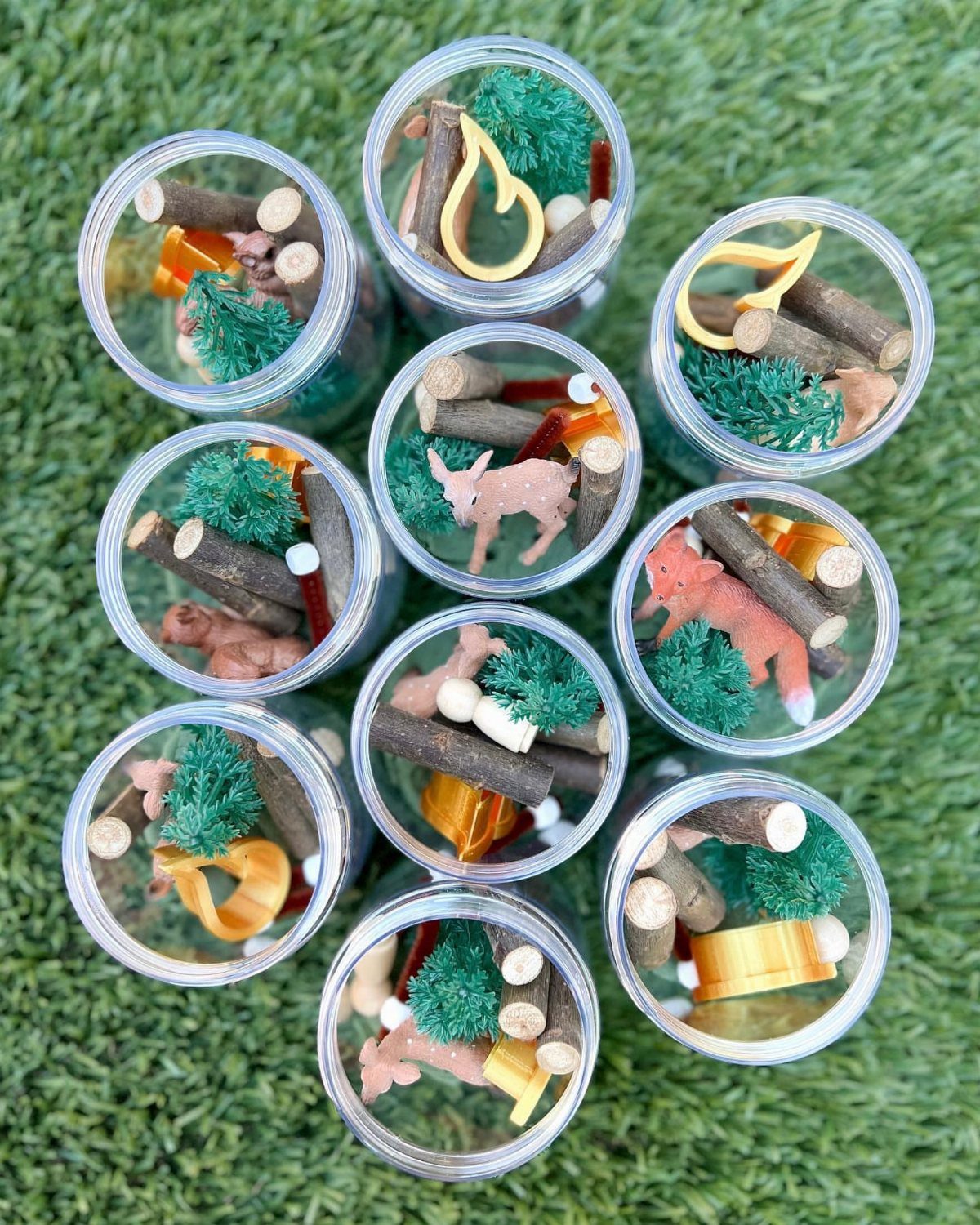 Clear plastic jars filled with miniature camping scenes on green grass.