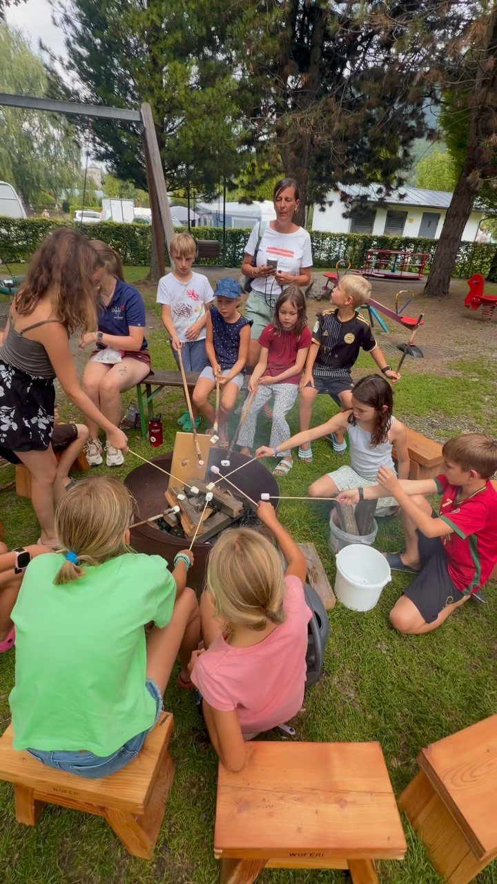 Children roasting marshmallows over a campfire using long sticks in a wooded area.