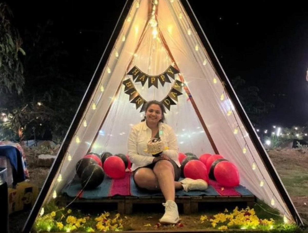 Woman sitting inside a decorated birthday teepee with string lights and balloons.