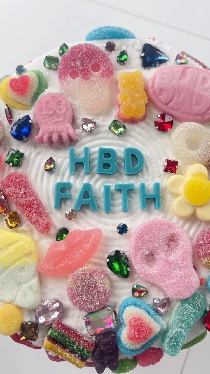White frosted cake topped with colorful gummy candies, gemstones, and blue birthday lettering.