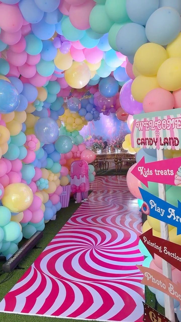 Pastel balloon tunnel and red spiral floor runner leading to a Candy Land party.