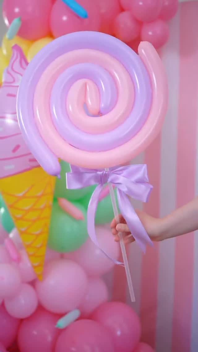 Giant lollipop decoration made of pink and purple balloons held by a hand.