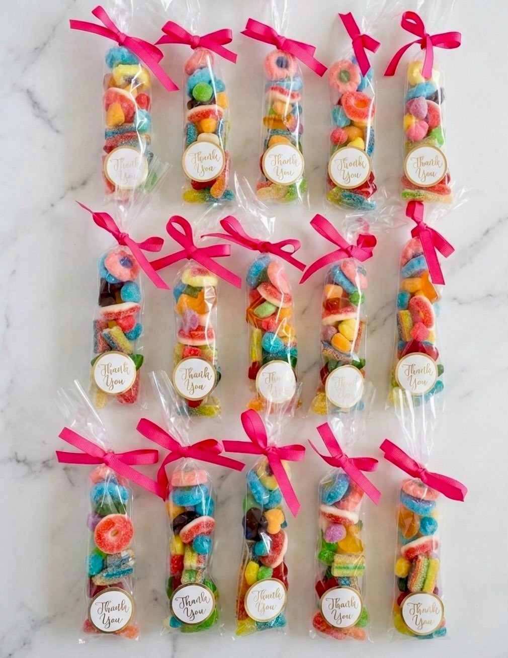 Clear bags of colorful gummy candies tied with pink ribbons and thank you labels.