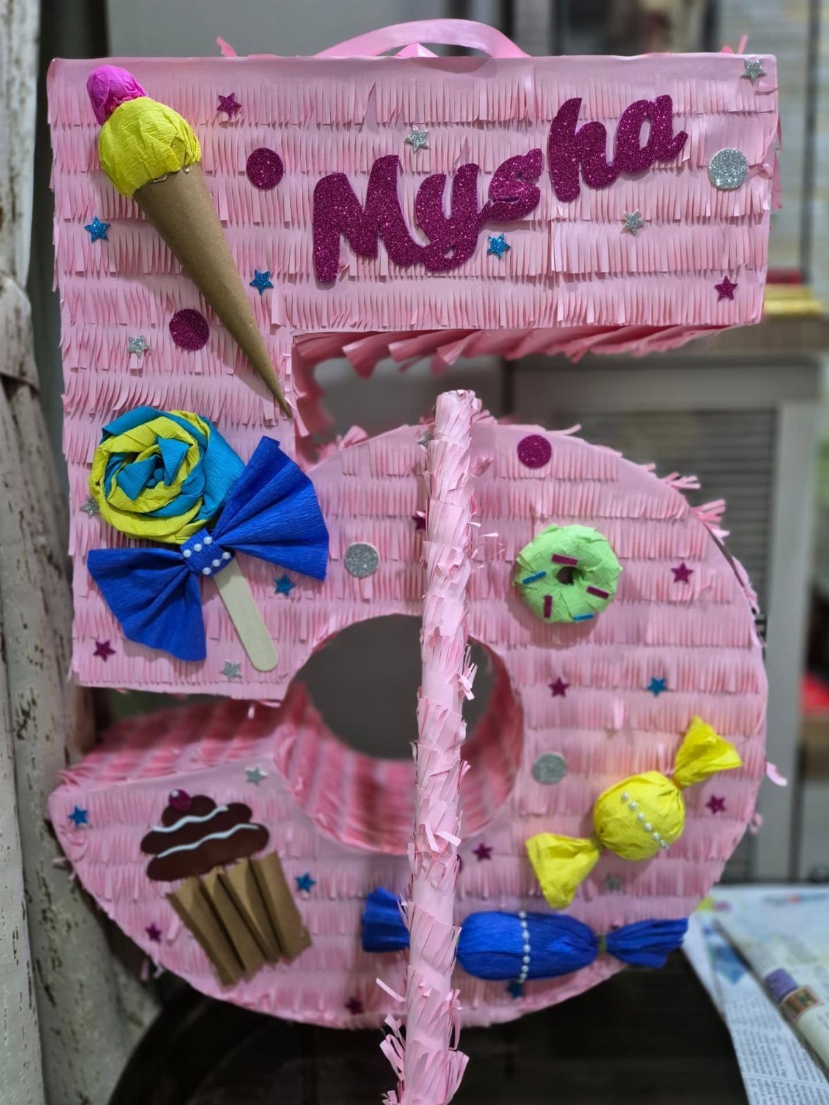 Pink number 5 piñata decorated with colorful candy shapes and glittery name.
