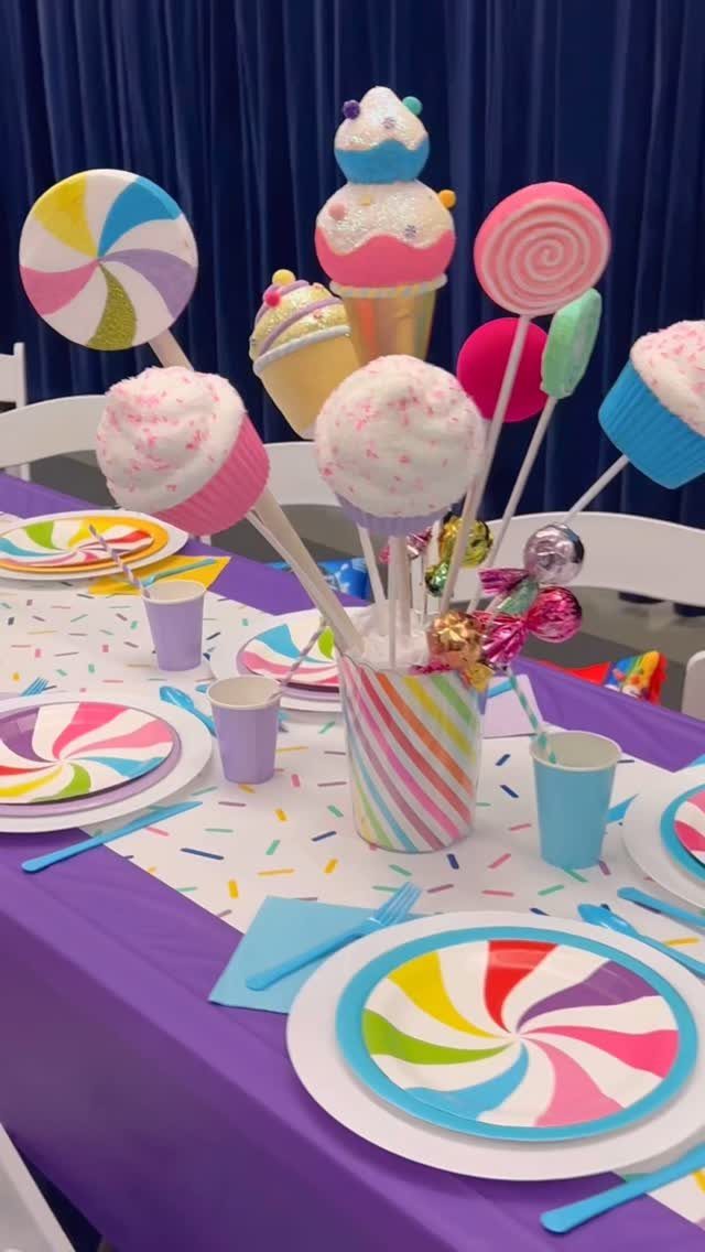 Candy themed party table with colorful swirl plates and oversized faux sweets centerpiece.