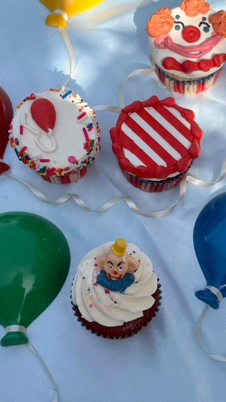 Carnival themed cupcakes with clown and balloon decorations on a white background