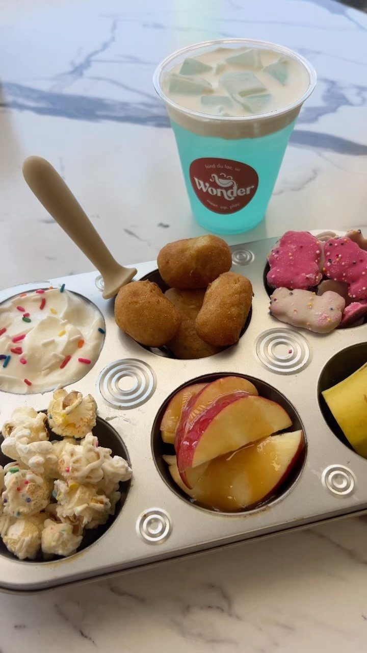 Sampler tray with popcorn, fruit, and sweets next to a blue iced drink