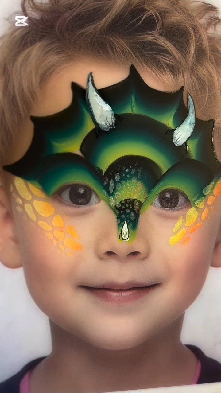 Young child with a detailed green and yellow dragon face painting design.